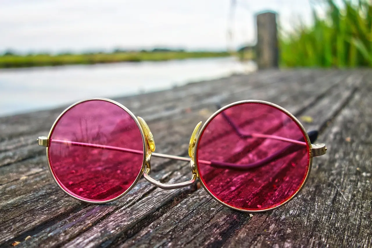 Runde solbriller med pink glas på et trædæk